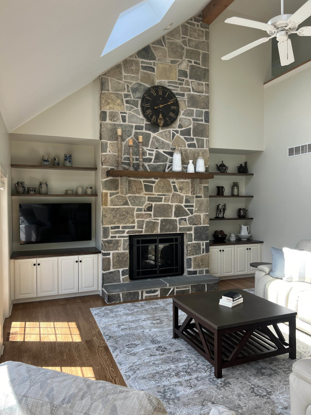 Custom-built-in cabinets and natural wood shelves frame the fireplace, blending storage with design while complementing the natural stone feature.