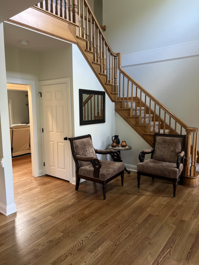 Matching the refinished flooring to the stair treads and railing stain unifies the main level and adds a polished, professional finish.