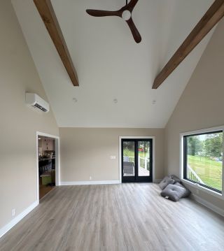 Reverse view of the vaulted Landenberg home addition showing exposed beams, ceiling fan, black-framed doors and oversized windows.