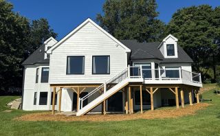 Rear view of white Landenberg home with finished lakefront addition and elevated deck.